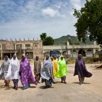A group of women walk along a street in front of the bombed out ruins of what was the Emir’s palace in Gwoza, Nigeria.   © UNHCR/Hélène Caux